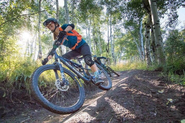 Woman mountain biking down hill with full gear on, smiling